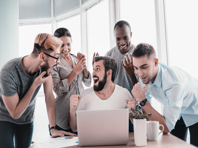 Five diverse business people rejoicing together over a laptop while working in office boardroom. Business team working on their business project together at office. They get a deal. Concept of success
