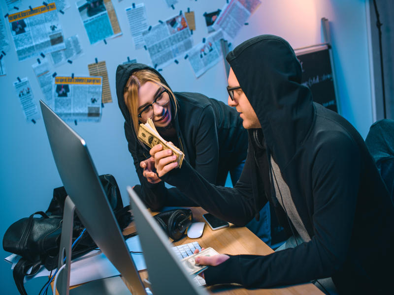 happy couple of hackers with stack of cash at workplace